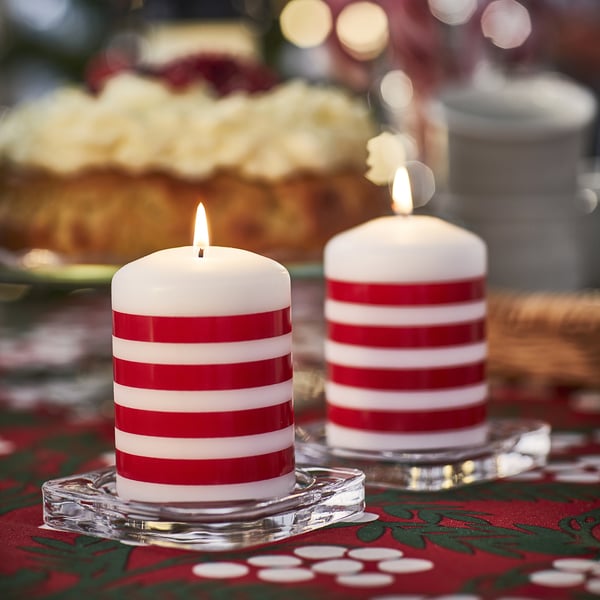 Two red and white striped VINTERFINT candles, lit, on glass holders. Holiday-themed table setting.