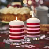 Two red and white striped VINTERFINT candles, lit, on glass holders. Holiday-themed table setting.