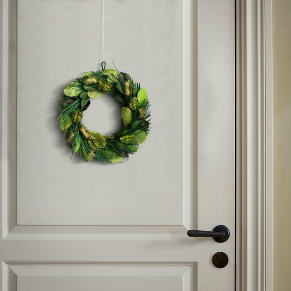 A green plant wreath hangs on a white door, adding natural decor and a welcoming touch.