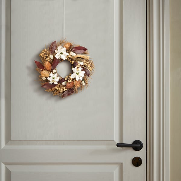Wreath of dried plants and white flowers on gray door with black handle.