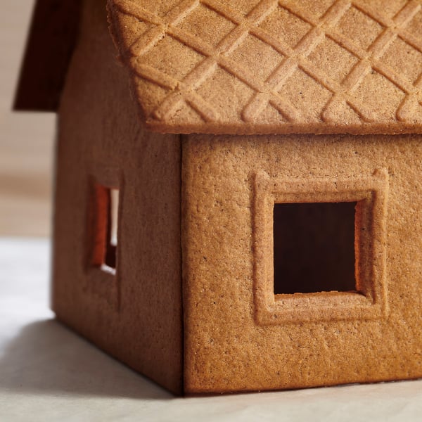Mini gingerbread house model, brown, textured roof, square windows.