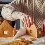 A person assembles gingerbread houses, using icing as glue on a table.