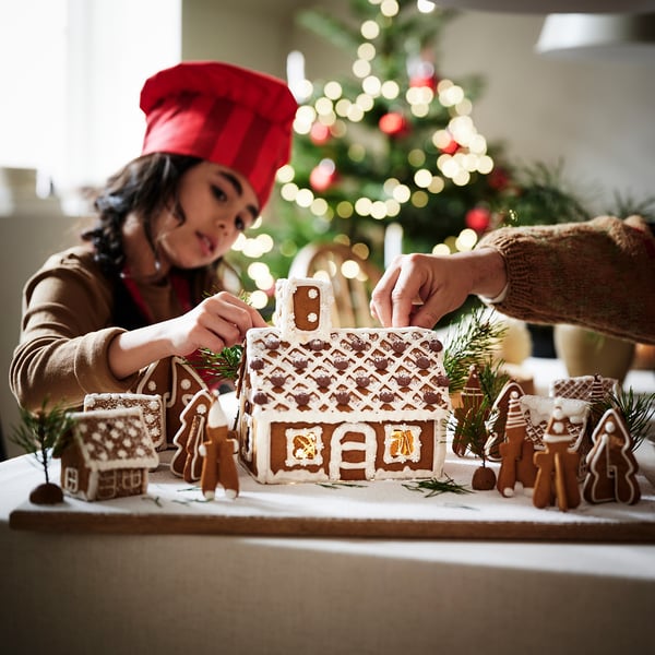 Person decorating gingerbread house, festive setting with christmas tree.