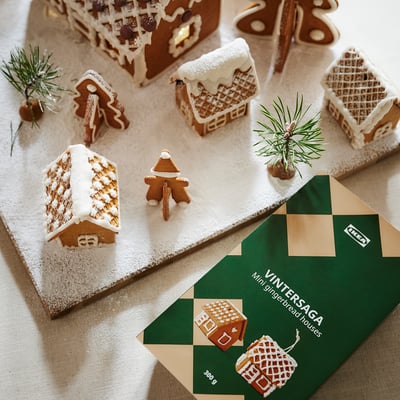 Gingerbread houses & person from IKEA VINTERSAGA, decorated with pine branches on snow, with a 300g packet.