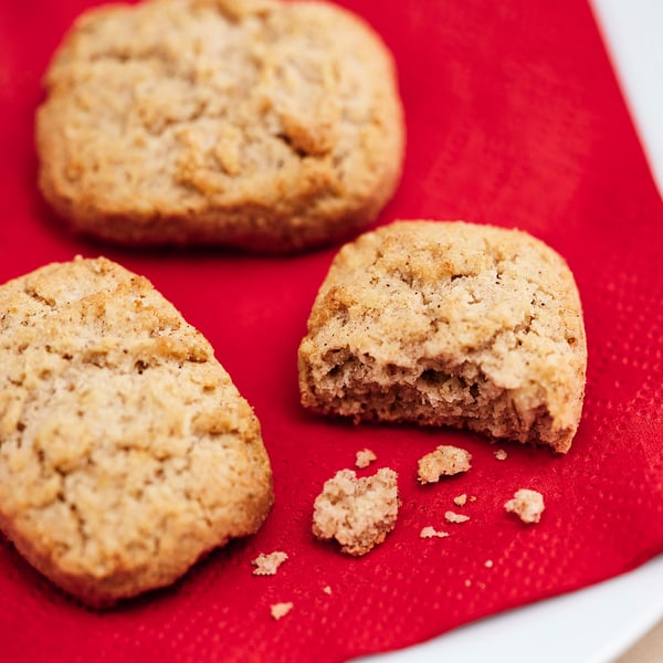 Three golden-brown cookies on red surface; one bitten.