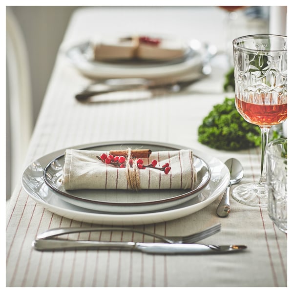 Elegant dinner setting with white plates, silverware, clear glass with red liquid. Striped beige napkins tied with twine and red berries on table.