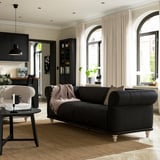 Cozy living room with VISKAFORS black sofa, white curtains, and kitchen in background.