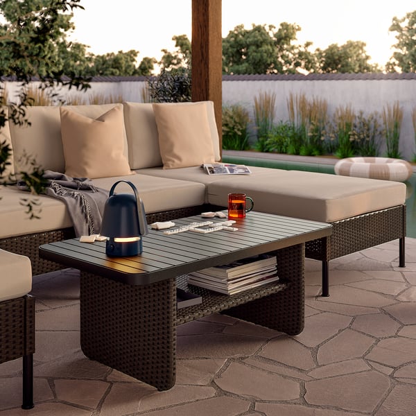 A VITTSKÄR outdoor lounge set in brown on a patio. A large sectional sofa with beige cushions, a dark coffee table, and a small side table.
