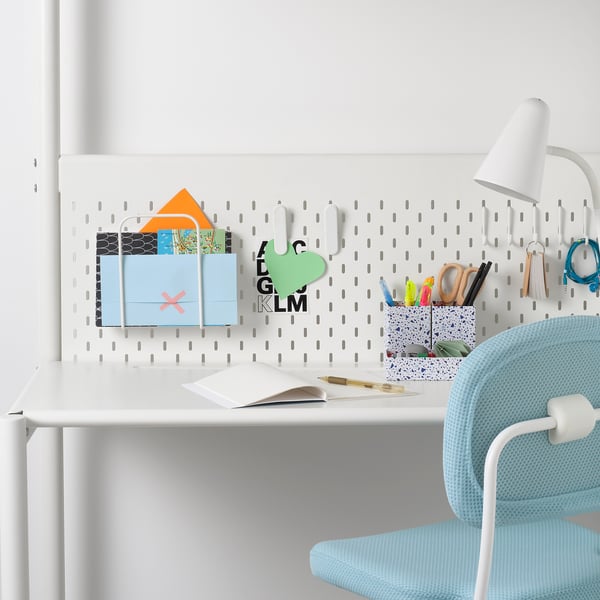 White desk setup with pegboard, boxes, blue chair, lamp, and accessories.