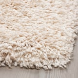 White shaggy rug, soft and plush, with varying yarn thickness, laid on wooden floor.