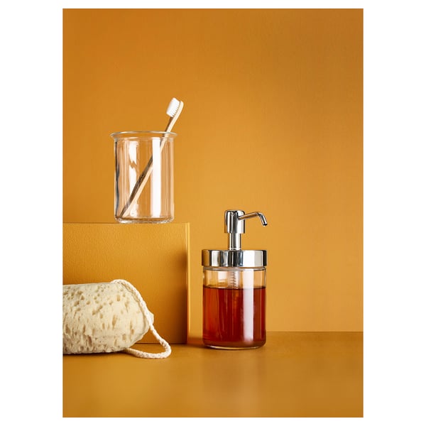 Clear glass VOXNAN bathroom set with soap dispenser, toothbrush holder, and loofah on yellow surface.