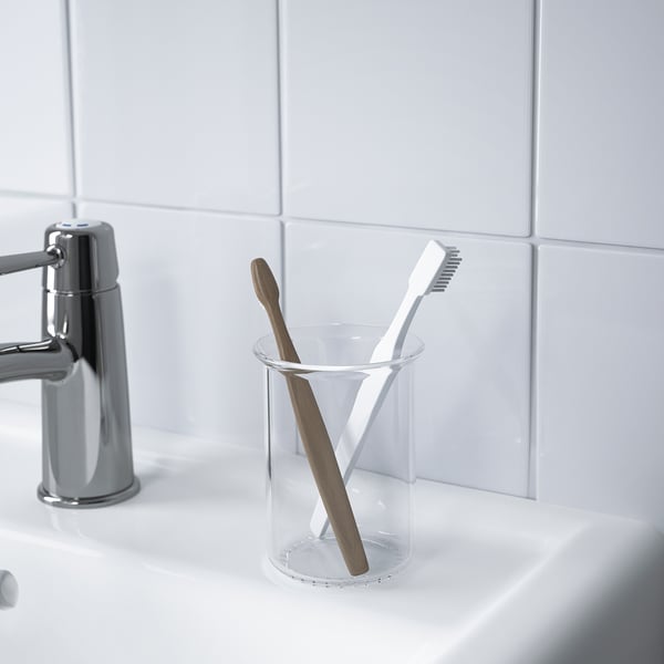Two toothbrushes in a clear glass holder, placed on a white sink near a chrome faucet.