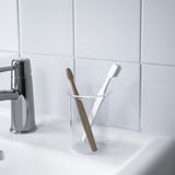 Two toothbrushes in a clear glass holder, placed on a white sink near a chrome faucet.