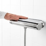 Hand adjusting VOXNAN shower mixer, featuring 38°c safety stop and cold touch technology, mounted on tiled wall.