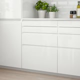 White glossy kitchen cabinets with modern, sleek design. Plants and items placed on top, making them appear taller.
