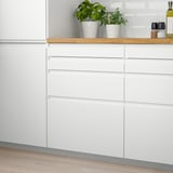 Modern white kitchen cabinets with wooden countertop, green plants, and small appliances. Smooth, minimalist design. Cabinets are larger than items.