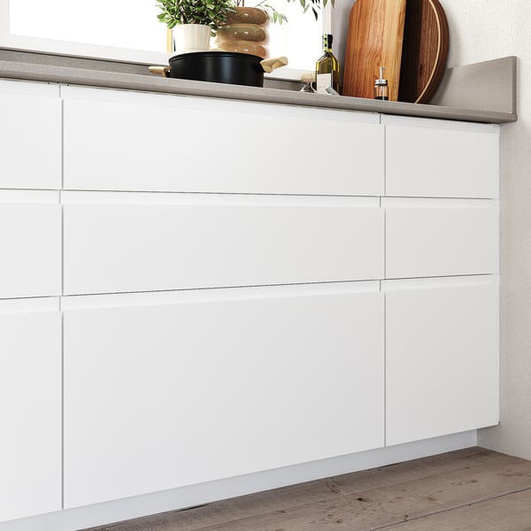 Modern white kitchen cabinets with minimalist design, smooth surfaces, and integrated handles; wooden floor.