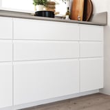 Modern white kitchen cabinets with minimalist design, smooth surfaces, and integrated handles; wooden floor.