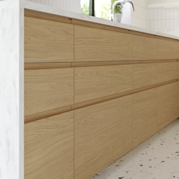 Modern kitchen with light brown oak cabinets, sleek handles, and marble countertop.