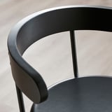 Black bar stool with curved backrest and armrest, craftsmanship details visible.
