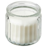 Ett ADLAD doftljus i en genomskinlig glasburk som innehåller vitt vax. Burken har en räfflad design och är cylindrisk i formen.