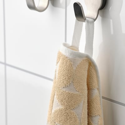 Beige handduk med strukturmönster hänger på silverkrok, mjuk och absorberande.