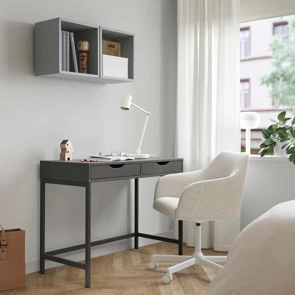 Modernt hemmakontor med ALEX svart skrivbord, justerbar lampa, grå stol och vägghylla. Stort fönster med gardiner släpper in naturligt ljus.