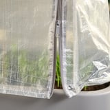 Ett växthusöverdrag, vitt, tillverkat av polyeten, med dragkedjor för åtkomst. Det skyddar växter från hårt väder.