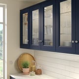 Mörkblått skåp AXSTAD med glasdörrar som visar upp glas och tallrikar som kompletterar den moderna köksdesignen.