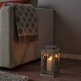 BEFÄSTA lykta lyser varmt bredvid soffan, gjord av glas och metall, och passar perfekt bredvid stora möbler.