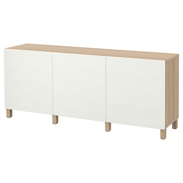 Ett vitt BESTÅ sideboard med tre dörrar och fyrkantiga ben. Den minimalistiska designen, en topp i ljust trä och ben i ek.