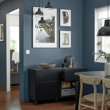 Svart sideboard med lådor och skåp, inramad väggkonst, hängande lampor, trägolv.
