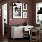 Vitt BESTÅ sideboard med hyllplan, marmoreffekt, mot vinröd vägg, under svarta lampor, med skål och dekor.