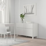 Minimalistiskt vardagsrum med skänken BESTÅ, växt, skål, skrivbord, stol, trädbild.