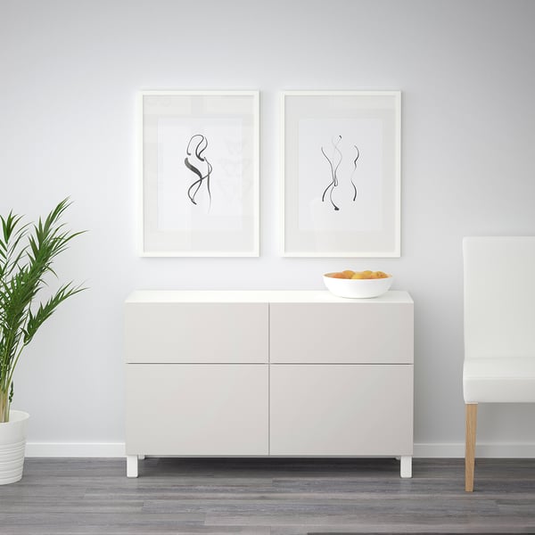 Vitt sideboard BESTÅ med två inramade konstverk och en skål med apelsiner.