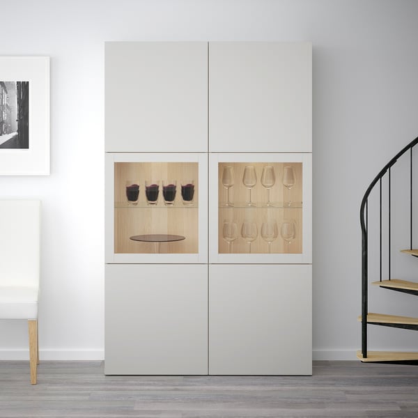 Vitt BESTÅ-skåp, med glasdörrar som visar vinglas och flaskor inuti. Display- och förvaringskombo med justerbara hyllplan.