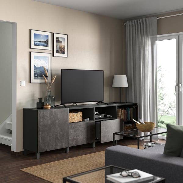 Modernt vardagsrum med BESTÅ tv-bänk, tv, foton, lampa, soffbord, böcker, grå gardiner, mörka trägolv, beige väggar, naturlig inredning.