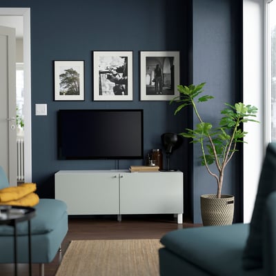 Modernt vardagsrum med grå väggar, blå tv-bänk, platt-tv, blå fåtöljer, inredning och grön växt.