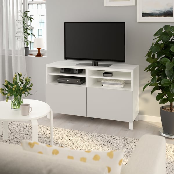 BESTÅ tv-bänk i vitt med tv, hyllor, växt och blommor.