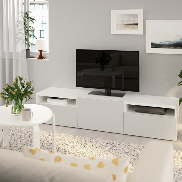 Minimalistiskt vardagsrum med tv-bänken BESTÅ, platt-tv, soffbord, blommig inredning och konst på neutrala väggar.