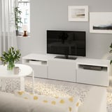 Minimalistiskt vardagsrum med tv-bänken BESTÅ, platt-tv, soffbord, blommig inredning och konst på neutrala väggar.