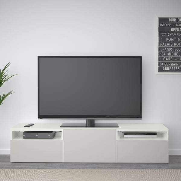 En modern vit BESTÅ-tv-bänk med en svart skärm-tv. Den har eleganta förvaringslådor och en minimalistisk design.
