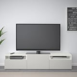 En modern vit BESTÅ-tv-bänk med en svart skärm-tv. Den har eleganta förvaringslådor och en minimalistisk design.