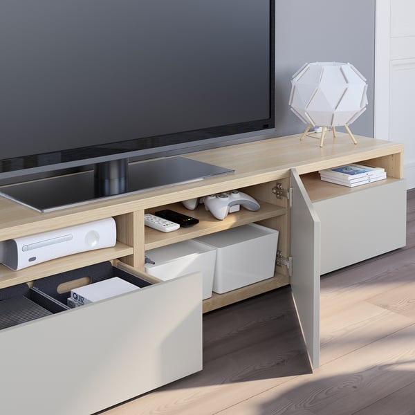 Tv-bänk i ljust trä med öppna lådor, som visar fjärrkontroll och kontroller, med plattskärms-tv på toppen.