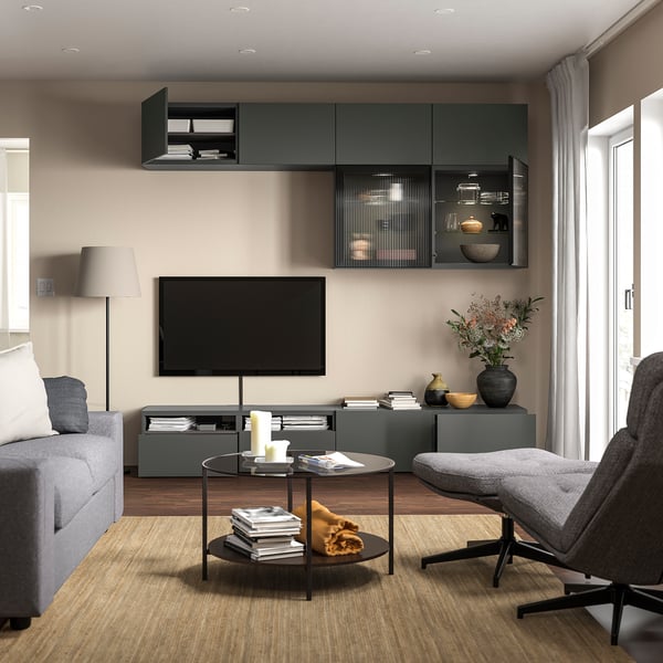 Modernt vardagsrum med grå tv-bänk BESTÅ, grå soffa, soffbord i glas och grå fåtölj. Tv monterad på vägg med förvaringshyllor.