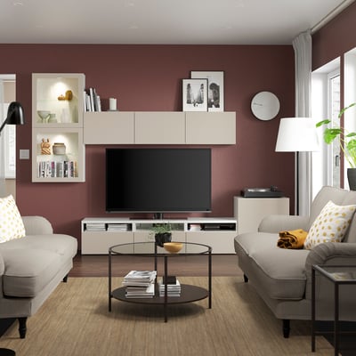 Vardagsrum med grå soffor, gula kuddar, svart soffbord, vit tv-möbel, vinröda väggar, dekorativa skåp, stort fönster och modern lampa.