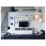 Modernt vardagsrum med tv-bänken BESTÅ, svart tv, grå soffa, taklampor och tavelvägg. Trappa och loft i bakgrunden.