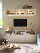 Modernt vardagsrum med BESTÅ-tv-enhet, som visar plattskärms-tv, dekorativa föremål och leksaker på beige matta.