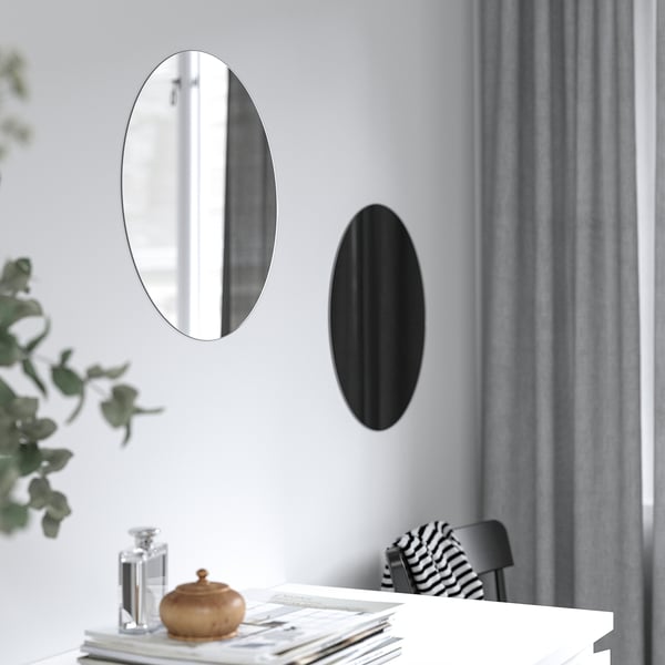 Två ovala speglar på väggen; En reflekterande, en svart, ovanför bordet med dekorativa föremål.