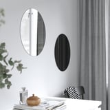 Två ovala speglar på väggen; En reflekterande, en svart, ovanför bordet med dekorativa föremål.